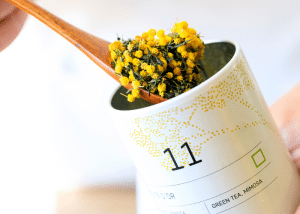 une cuillère en bois qui prend des grains du thé n°11 avec des grains de mimosa